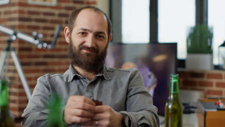 Portrait of caucasian man drinking beer and playing cards game, having fun with cheerful friends....