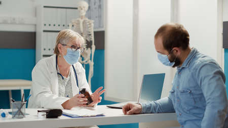 Female physician giving bottle of pills to sick man at checkup visit, meeting in cabinet during...