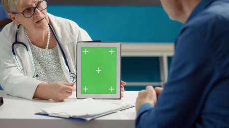 General practitioner and patient looking at greenscreen background on digital tablet in office. Isolated mockup template with blank copyspace and chroma key display at medical examination.の写真素材