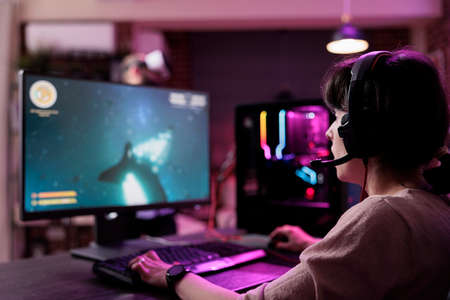 Modern person playing video games online on live stream, using computer and neon lights in living...