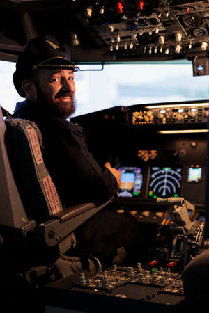 Portrait of smiling male captain flying airplane with panel command in jet cabin, using dashboard...
