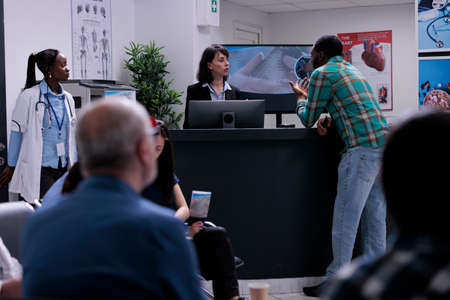 African american patient talking with private clinic receptionist registering for doctor appointment...