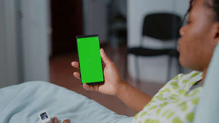 Close up of patient holding smartphone with green screen in hospital ward. Mobile phone with isolated background and mockup template with chroma key on screen. Person with phoneの写真素材
