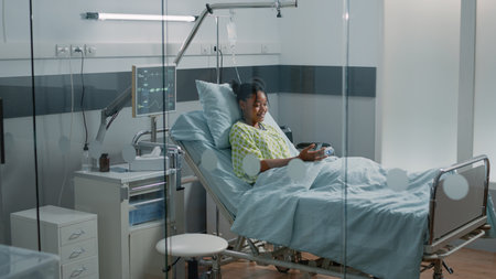 Ill patient holding mobile phone to talk on video call communication with friends. Woman with disease using online video conference to have conversation with family in hospital ward.の写真素材