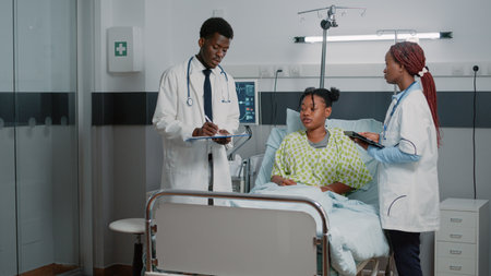 Man and woman doctors consulting young patient with disease. Medical team of people using tablet and documents to check healthcare treatment and medicine progress to heal person.の写真素材