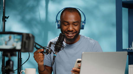 Blogger reading good news from smartphone on camera, recording video for channel. Influencer feeling joyful while filming vlog with microphone and equipment for social media careerの写真素材