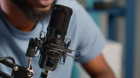 Close up of black vlogger using microphone on podcast. Social media influencer talking to subscribers on camera for vlog. African american blogger working with modern equipment and gear.の写真素材
