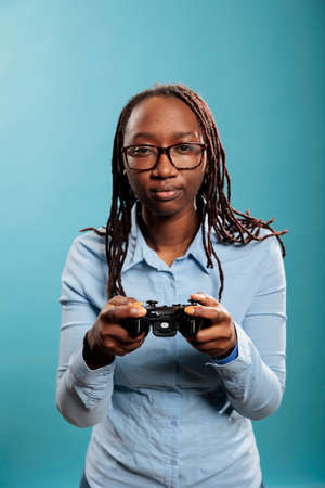 Smiling fun woman playing online videogames on gaming console with controller on blue background....