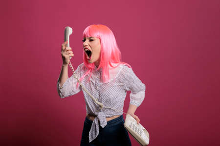 Crazy funky person screaming at landline phone call on camera, posing and talking on retro vintage telephone. Having remote conversation with stationary cord phone, trendy woman in studio.の写真素材