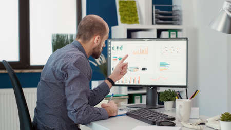 Company accountant analyzing business charts and sales data on computer monitor, using e commerce...