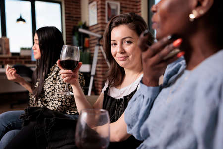 Joyful multiethnic close friends celebrating birthday event at home while sitting in living room. Diverse group of people in living room enjoying relaxing time together while bonding.の写真素材