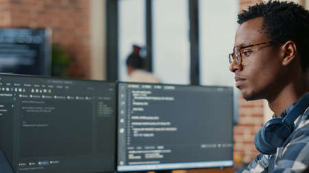 Portrait of focused software developer writing code arranging glasses sitting at desk in data room. System engineer programming user interface in busy artificial intelligence developing agency.の写真素材