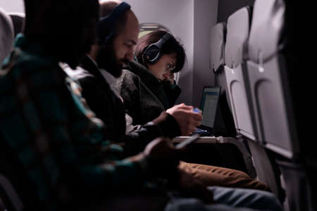 Multiethnic group of passengers flying abroad by airplane jet, using modern devices during international plane transportation. Travelling in economy class with airways flight trip.の写真素材
