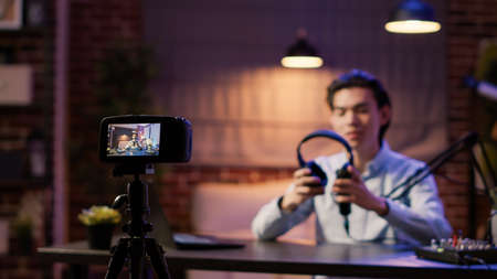 Camera recording video of vlogger doing product review with wireless headphones for channel content. Recommending audio headset on social media podcast episode, live broadcast show.の写真素材