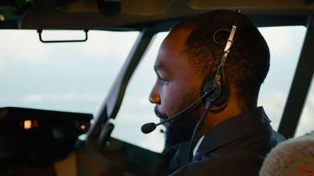 African american copilot taking off with airplane captain, using aircraft command on dashboard in cabin. Pressing power buttons and throttling engine, wearing headset. Close up.の写真素材
