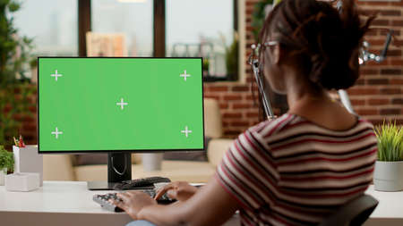 Female freelancer looking at computer with greenscreen, working remotely. Businesswoman using isolated mockup background with blank copyspace template and chroma key on monitor display.の写真素材