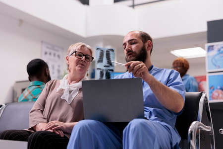 Male nurse explaining x ray diagnosis to old woman in hospital reception lobby, talking about...