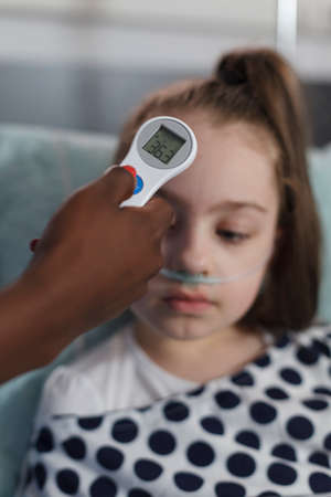 Close up shot of pediatric hospital nurse measuring sick little girl body temperature using...