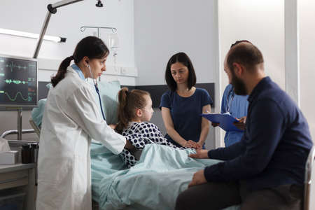 Expert pediatrist checking sick girl health condition using stethoscope while parents sitting...