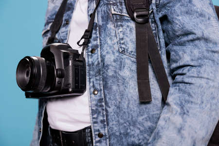 Close up shot of photography enthusiast having professional DSLR camera while standing on blue...