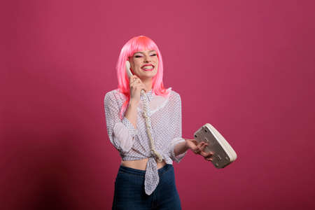 Beautiful woman with pink hair talking on landline phone call, chatting on retro telephone cord line...