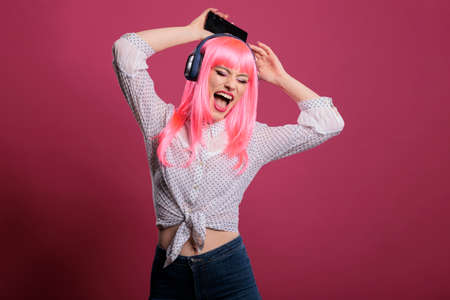 Positive person with pink hair having fun with mp3 music, listening to radio songs on headphones. Doing dance moves and enjoying audio sound, feeling relaxed and happy. Cool style.の写真素材
