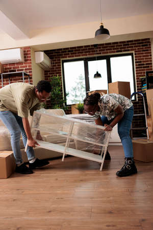 Husband and wife moving in new apartment together, unpacking furniture to decorate household....