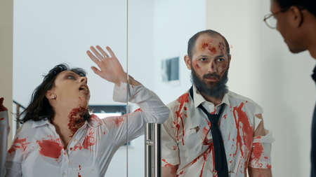 Mindless creepy monsters with deep scars trying to enter inside office workspace. Apocalyptic spooky brain-eating monsters looking for new victims while rubbing their faces on glass door.の写真素材