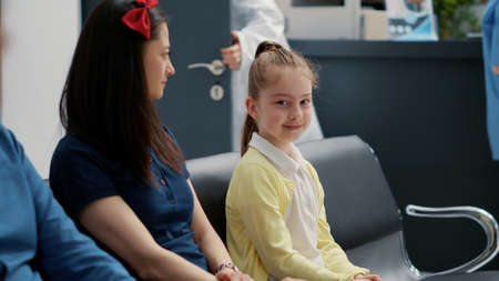 Portrait of little girl waiting with mother at hospital reception lobby, having medical consultation...