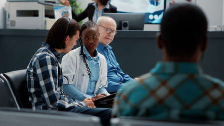 Female general practitioner consulting asian patient in waiting area lobby to give sickness...