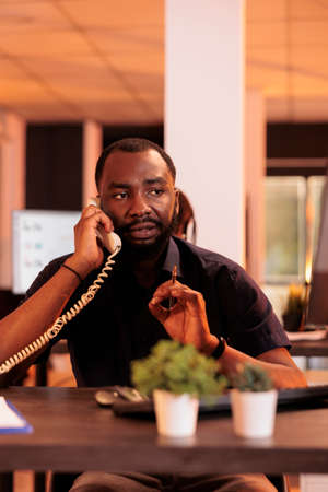 Male freelancer talking to people on landline phone, answering call to discuss about research information for report presentation. Chatting on office telephone line to do company paperwork.の写真素材