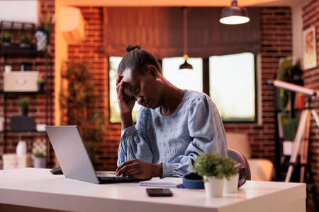 Overworked young female freelancer working on laptop in modern home office, burnout and workload...