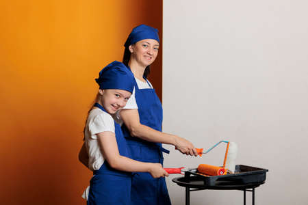 Portrait of people painting walls with orange, using paintbrush and tools to redecorate home...