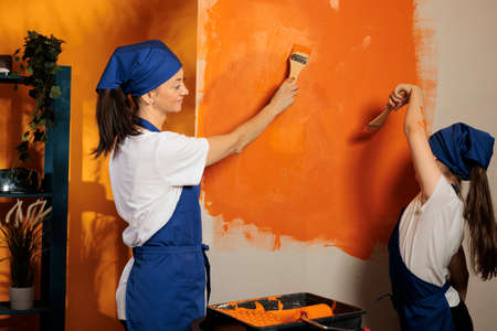 Adult with child painting orange walls with color paint and renovating tools or brush. Family having fun with diy redecoration equipment, using paintbrush to renovate apartment interior.の写真素材