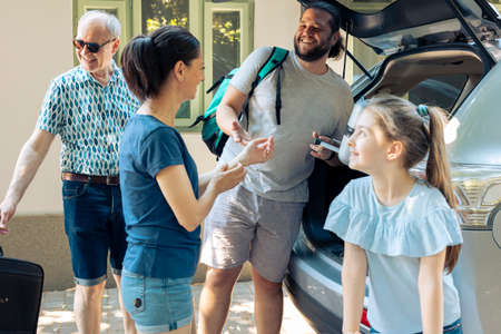 Caucasian family travelling on journey trip, putting bags and trolley suitcase in automobile trunk...