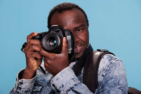 Photography enthusiast taking photo with DSLR camera while standing on blue background. Professional...