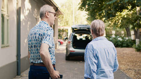 Senior couple putting luggage in car trunk while getting ready for holiday trip. Cheerful elders going on retirement voyage while having heavy baggage and travel trolley.の写真素材