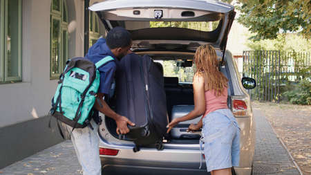 People putting baggage and trolleys inside car while getting ready for field trip departure. African...