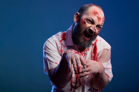 Dangerous looking halloween zombie attacking camera over blue background, brain eating scary corpse with bloody wounds. Frightening cruel monster with eerie apocalyptic look being creepy.の写真素材