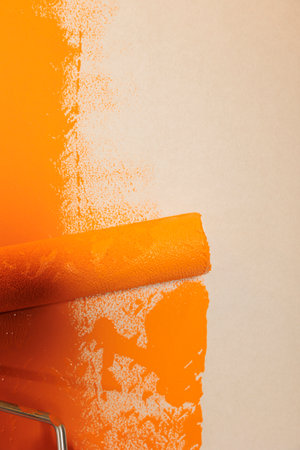 Rolling brush with orange paint to renovate and redecorate apartment walls, changing surface color with dye. Using round paintbrush with bristles and container with liquid to repaint. Close up.の写真素材