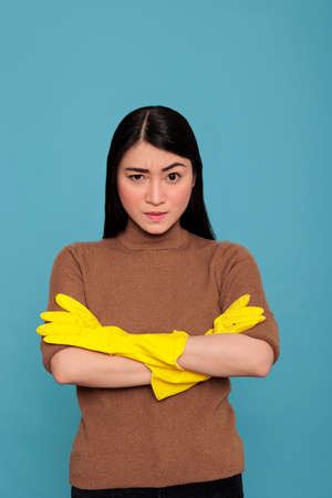 Asian tired angry and frustrated asian housekeeper at work wearing yellow glove against a blue...