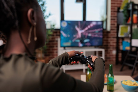 African american woman holding joystick to play shooting video games, enjoying party with beer and...