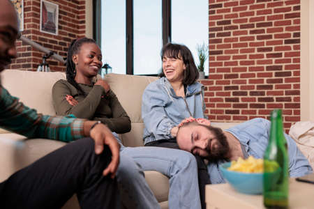 Multiethnic group of friends having fun and laughing together at house party with beer bottles and...