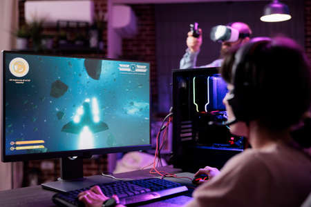 Woman playing shooter video games championship on pc, in living room with neon lights. Female gamer...
