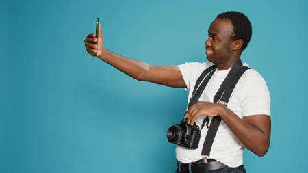 Photographer taking pictures using smartphone in studio, holding professional camera to pose. Capturing images with dslr lens and photography equipment, leisure fun activity. Focused view.の写真素材