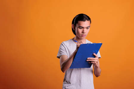 Young asian man taking notes in clipboard, serious student writing in notepad. Focused person...