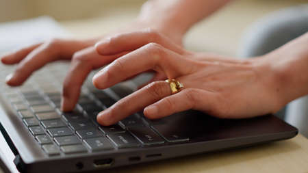 Close up of woman hands working on laptop. Person answering emails on modern portable computer while doing remote work at home while sitting on sofa in living room. Handheld shotの写真素材