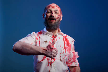 Halloween zombie man giving thumbs up in front of camera, scary aggressive monster showing okay like sign of approval in studio. Spooky creepy devil corpse with ugly scars and wounds.の写真素材