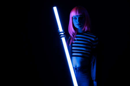 Portrait of stylish person holding purple neon light glowing in dark, having fun with fluorescent...