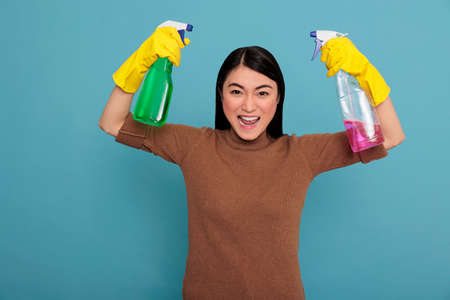 Happy excited and smiling asian housewife raising arms and showing biceps isolated blue background, Housewife worker, Cleaning home concept, Positive woman feeling energetic cheerful and gladeの写真素材